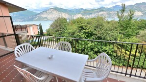 A balcony with a white table and chairs, overlooking a mountainous landscape and a body of water.