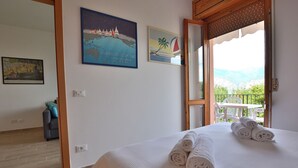 A hotel room with a bed, towels, a painting of a sailboat, and a view of mountains through the window.
