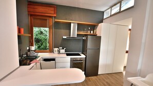 A modern kitchen with a built-in oven, a stainless steel refrigerator, and a window with blinds.
