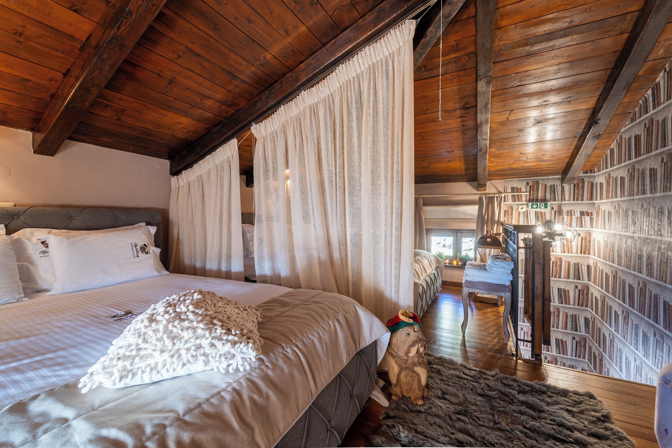 Une chambre à coucher avec un grand lit, un plafond en bois, une bibliothèque et un chien portant un chapeau.