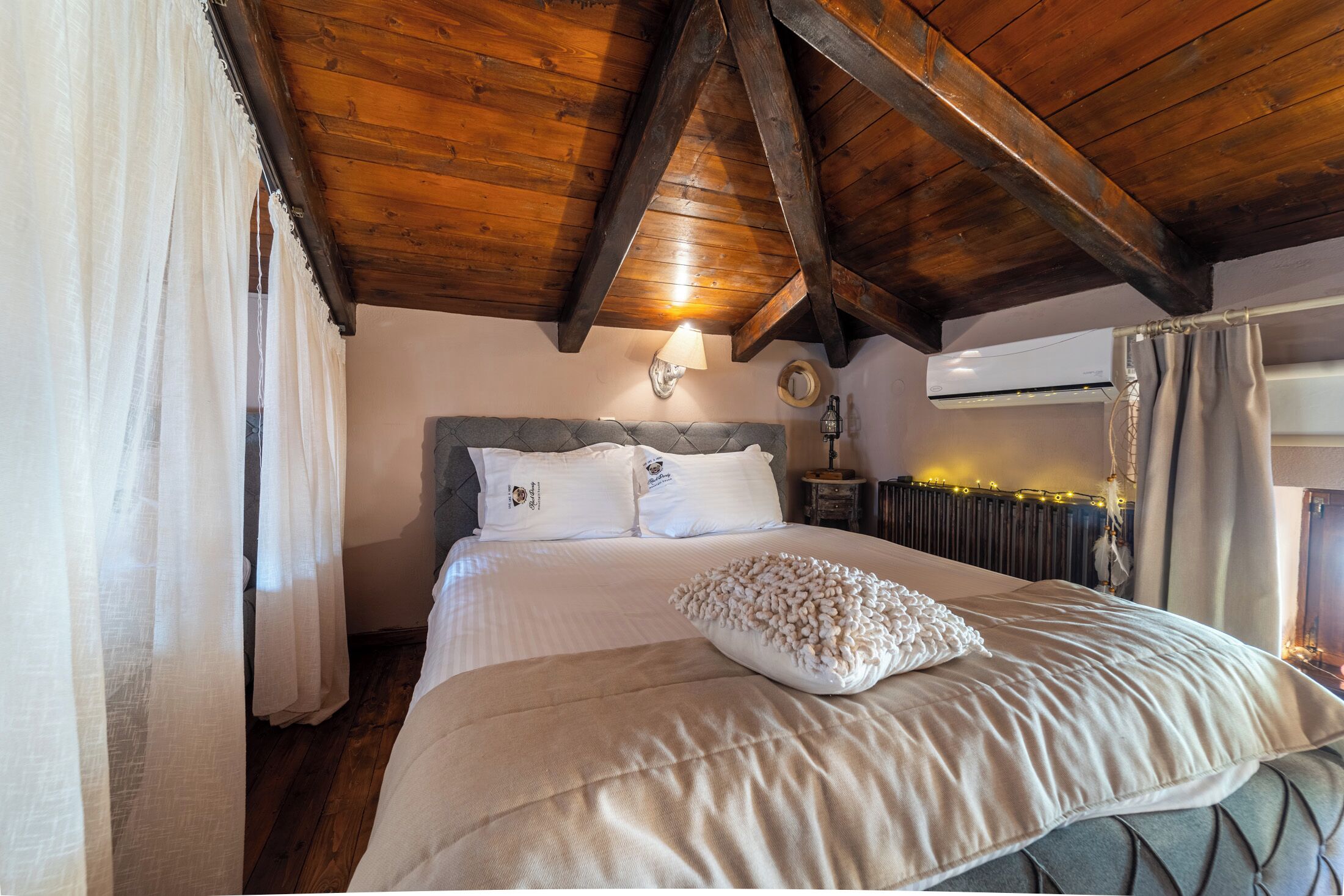 A bedroom with a wooden ceiling, a bed with white bedding, a headboard, and a wall-mounted lamp.