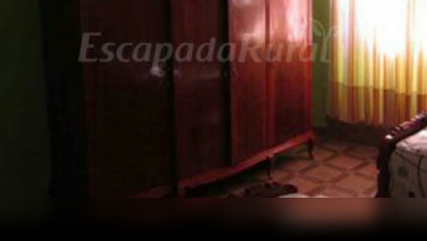 A room with a large wooden wardrobe, a bed with a headboard, and a window with curtains.