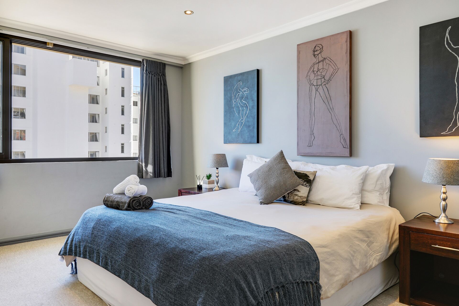 Una habitación de hotel moderna con una cama grande, una mesita de noche con lámpara y obras de arte en las paredes.