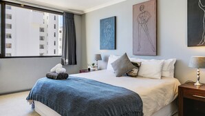 Una habitación de hotel moderna con una cama grande, una mesita de noche con lámpara y obras de arte en las paredes.