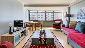 Una sala de estar moderna con comedor, un sofá rojo y un amplio ventanal con vistas a la ciudad.