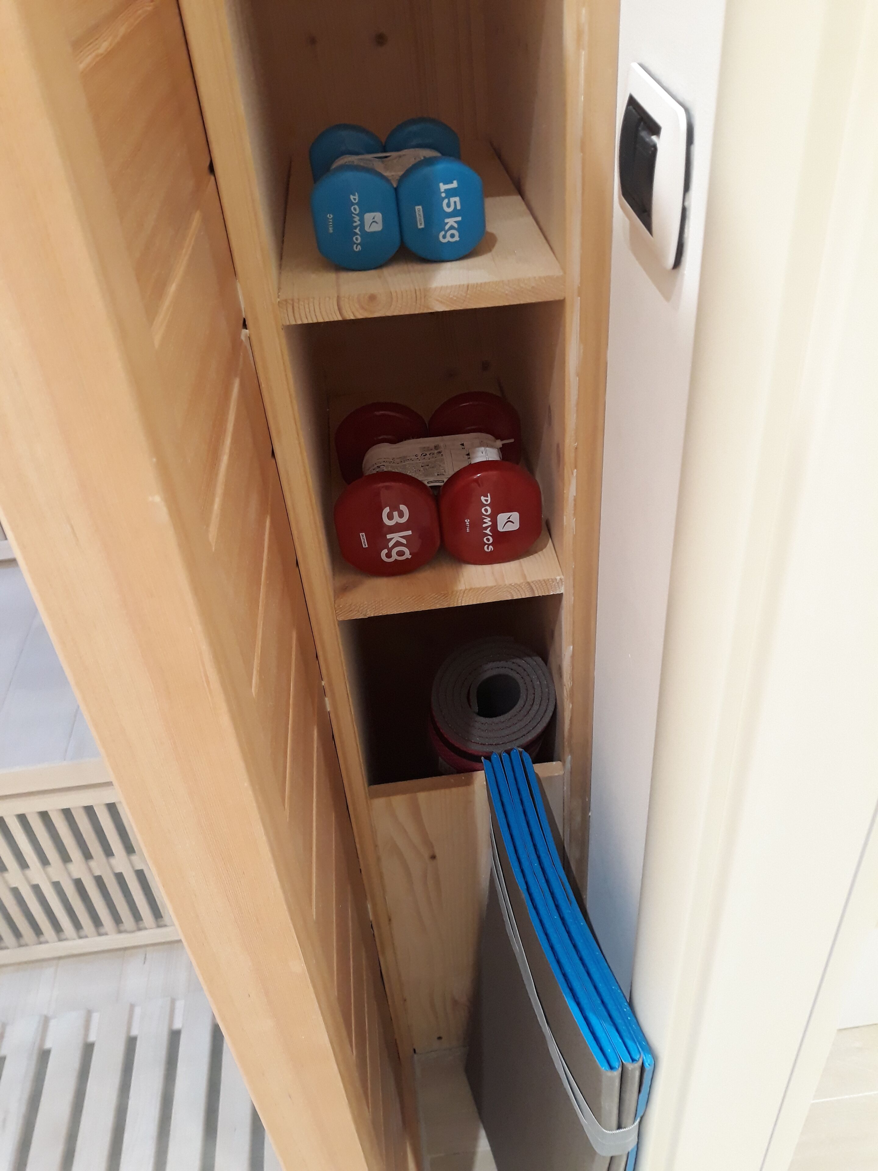 Ein Holzregal mit Gewichtsscheiben, beschriftet mit 1,5 kg und 3 kg, sowie ein blaues Widerstandsband.