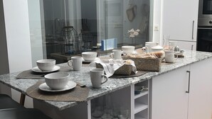 Eine moderne Küche mit weißen Schränken, einer Granitarbeitsplatte und einer Glasrückwand. Auf der Arbeitsplatte befinden sich verschiedene Küchenutensilien, darunter Schüsseln, Tassen und ein Wasserkocher.
