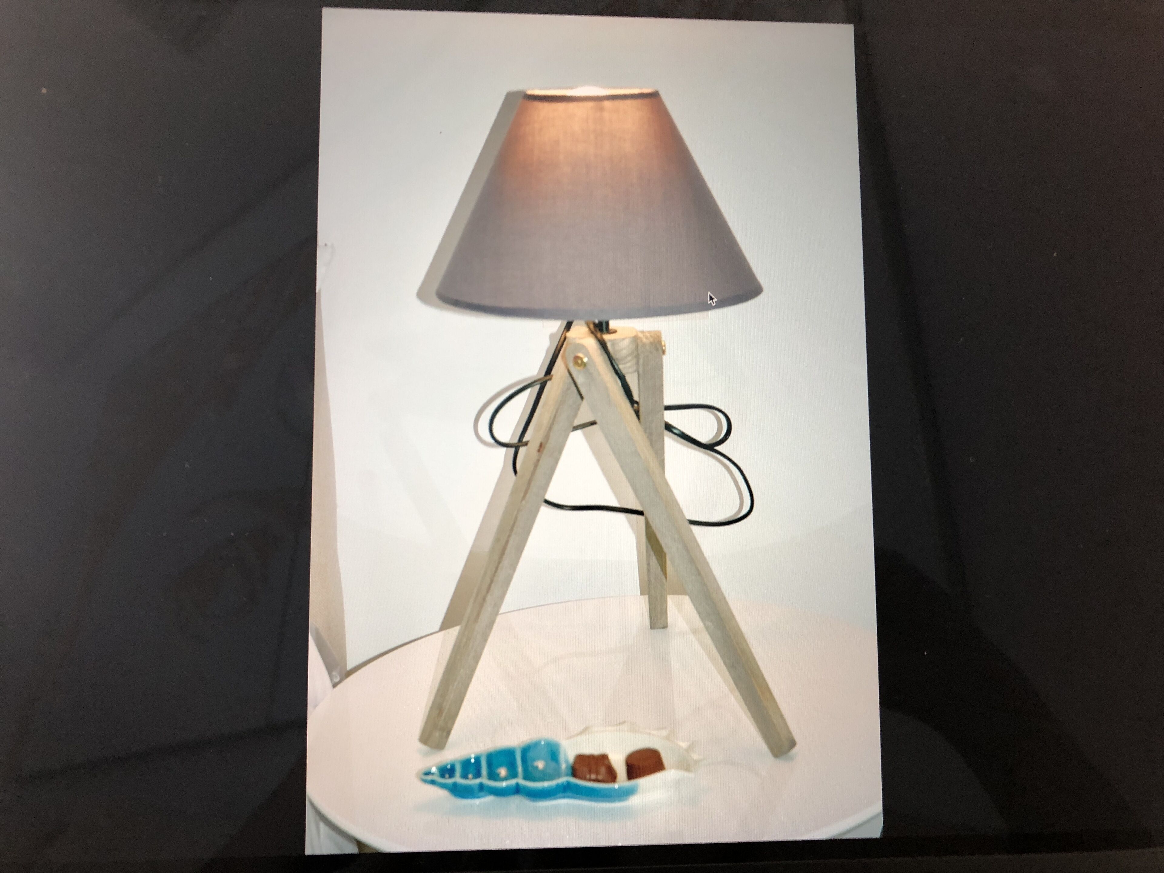 Una lampada con un paralume conico, un fusto in legno e un oggetto decorativo blu sul pavimento.