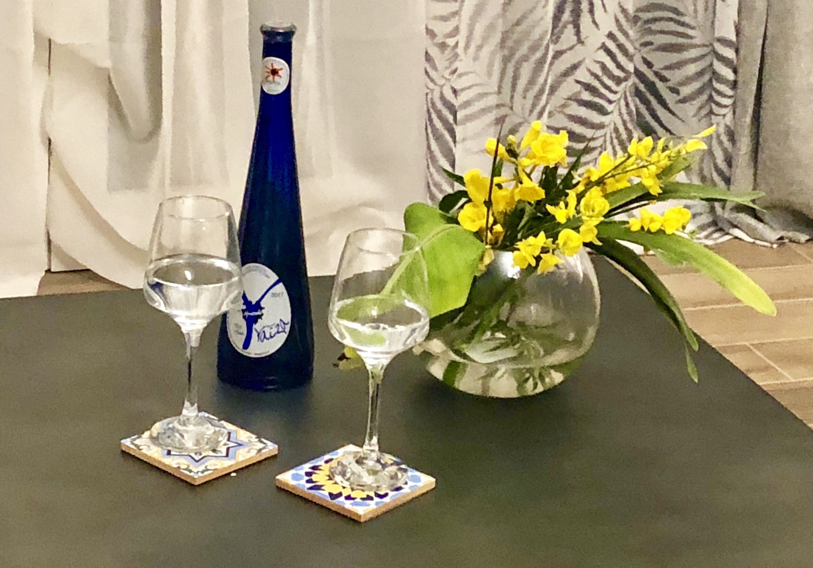 Ein Tisch mit zwei Weingläsern, einer Flasche und einer Vase mit gelben Blumen.