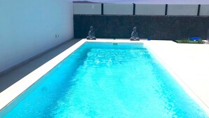 Ein rechteckiger Pool mit klarem, blauem Wasser, umgeben von einer weißen Liegefläche und einer dunklen Steinmauer.