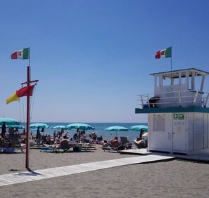 Una spiaggia con una torretta di salvataggio, ombrelloni e persone che si rilassano.