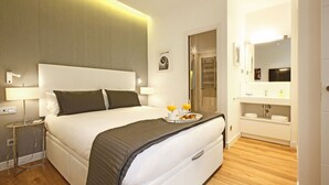 Et moderne hotelværelse med en stor seng, sengeborde med lamper, et bakke med morgenmad og et badeværelse med spejl og vask.