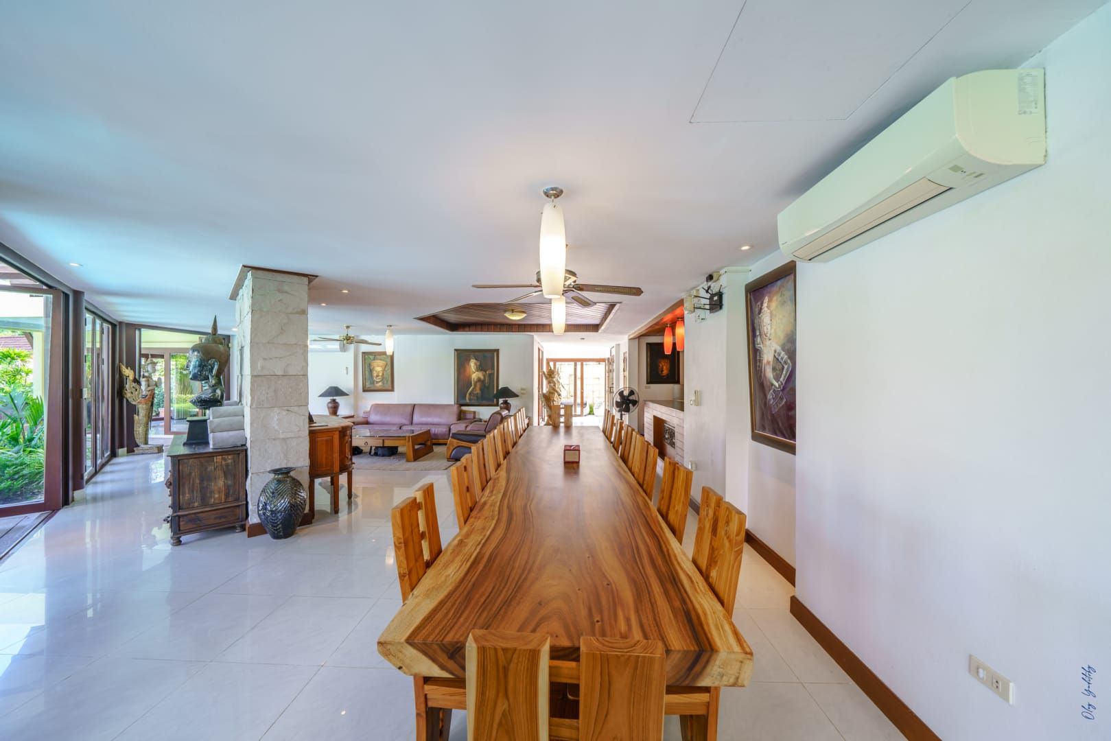 A spacious dining area with a long wooden table and chairs, a ceiling fan, and a view of the outdoors.