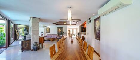 A spacious dining area with a long wooden table and chairs, a ceiling fan, and a view of the outdoors.