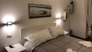 A hotel room with a bed, a bedside table with a phone, a wall-mounted light, a painting, and a shower curtain. - La mia struttura (Palermo,)