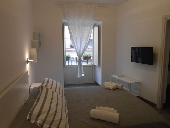 A bedroom with a bed, a TV, a window with curtains, and a balcony view.