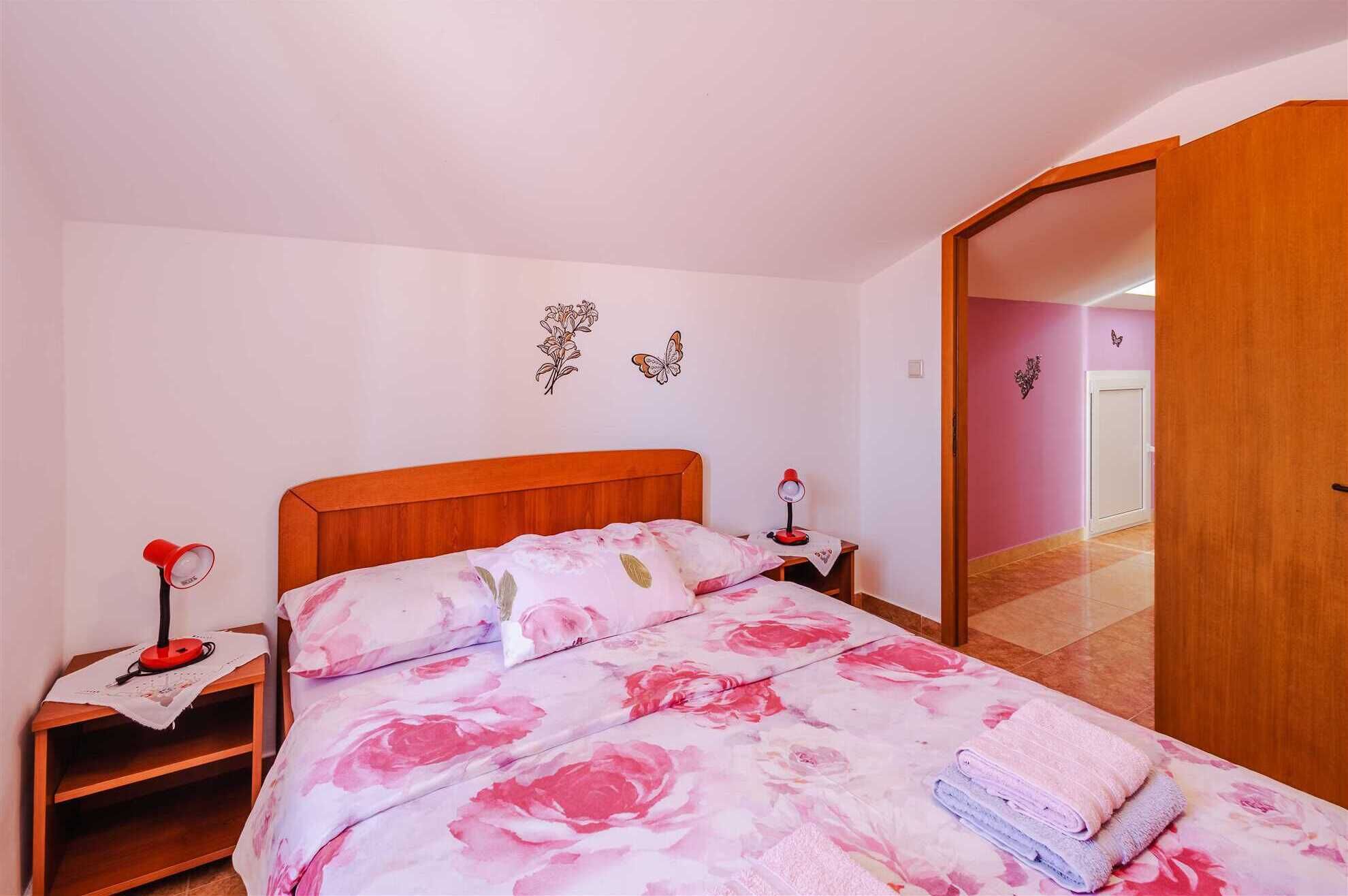 Ein Schlafzimmer mit einem hölzernen Bett, floraler Bettwäsche, einem Nachttisch mit Lampe und einer Tür zu einem anderen Raum.