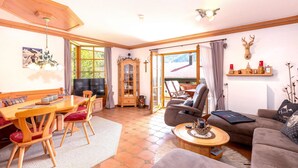 A cozy living room with a wooden dining table, red cushioned chairs, a brown sofa, and a fireplace. - Ferienwohnung Elisabeth, 90 qm für 2-4 Personen (Reit im Winkl)