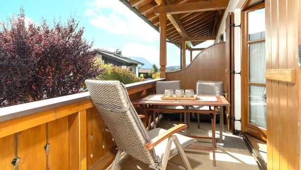 A wooden deck with a table and chairs, a view of the sky, and a building in the background. - Ferienwohnung Elisabeth, 90 qm für 2-4 Personen (Reit im Winkl)