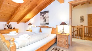 A bedroom with a wooden ceiling, a bed with white linens, two bedside tables with lamps, and a wooden staircase. - Ferienwohnung Elisabeth, 90 qm für 2-4 Personen (Reit im Winkl)