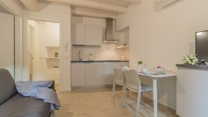Una cocina moderna con armarios blancos, una mesa de comedor con sillas y un sofá gris en una sala de estar luminosa.
