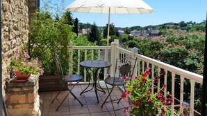 A balcony with a white umbrella, two metal tables, and chairs, surrounded by potted plants and flowers.