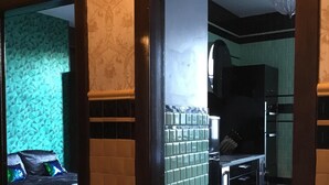 Ein Zimmer mit strukturiertem Wandpapier, einem Bett mit dunkler Bettdecke und einer gefliesten Spritzwand in der Küche.
