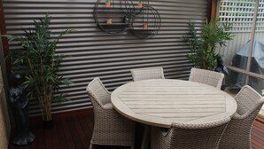 A round wooden table with wicker chairs, surrounded by potted plants, against a corrugated metal wall. - Church St - Conveniently Located in the Hart of Bright (Bright)