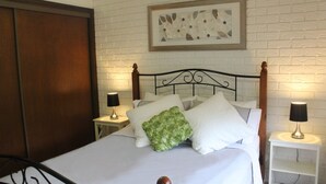A neatly made bed with white linens and a green floral pillow, flanked by two bedside tables with lamps, against a white brick-patterned wall. - Church St - Conveniently Located in the Hart of Bright (Bright)