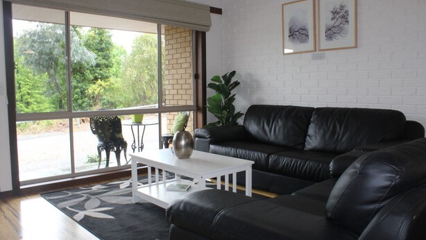A modern living room with a black leather sofa, a white coffee table, and a large window with a view of greenery. - Church St - Conveniently Located in the Hart of Bright (Bright)