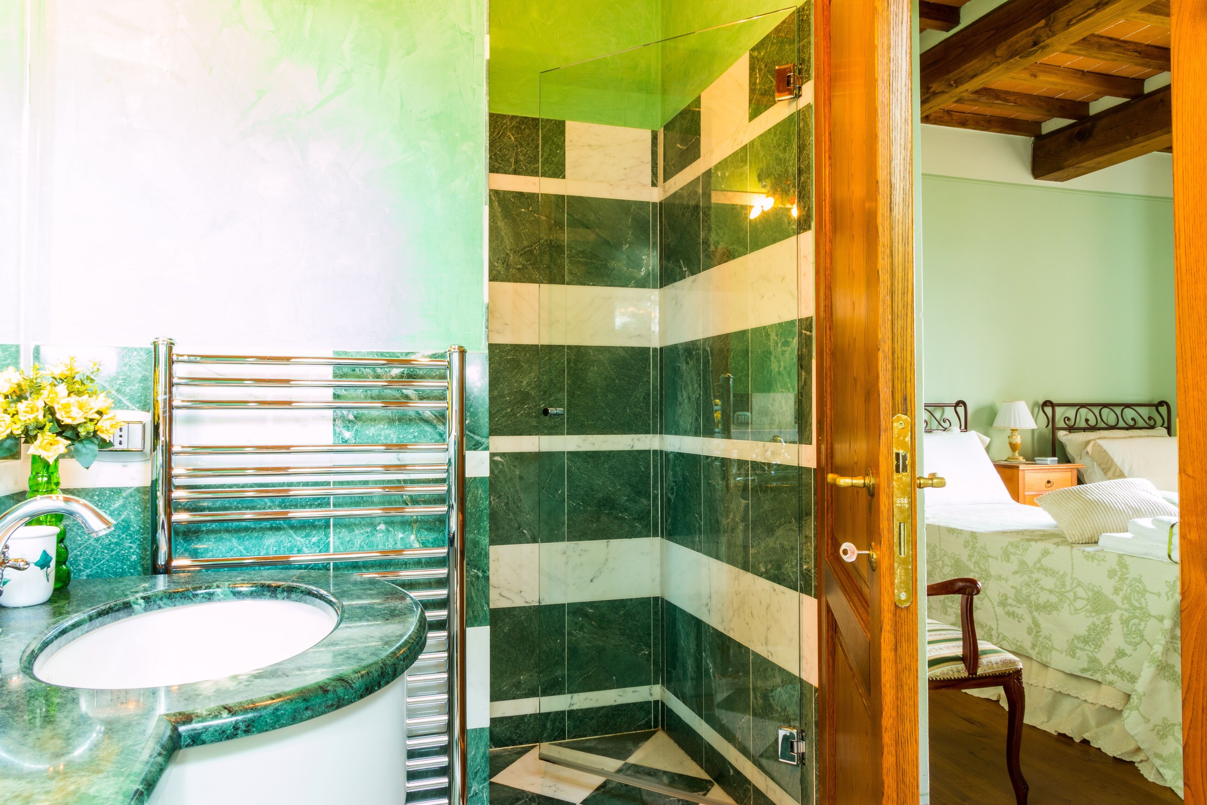 A bathroom with a sink, shower, and a bed in the adjacent room.