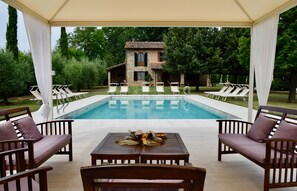 A pool area with lounge chairs and a table with flowers, surrounded by greenery and a stone building.