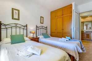 Ett hotellrum med två sängar, en garderob i trä och ett badrum som syns genom en öppen dörr.