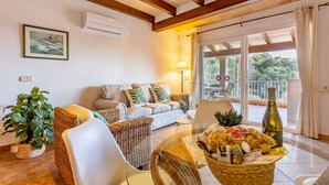 A living room with a sofa, wicker chairs, a glass table with a basket of snacks, a bottle, and a potted plant. - Es Recer by dracmallorca (Santanyi)