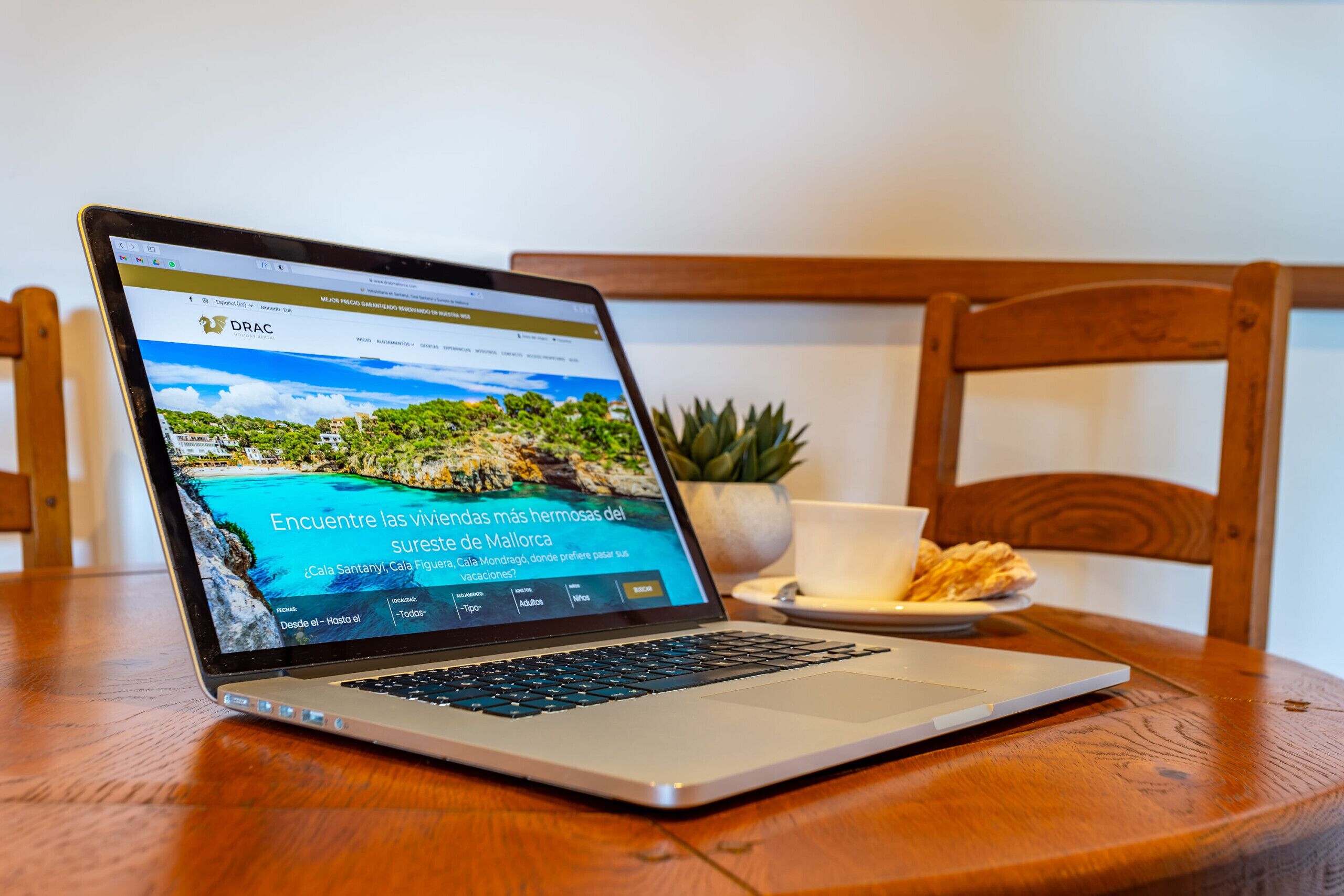 Un ordinateur portable est posé sur une table en bois, et son écran affiche le site web d’un hôtel avec une vue panoramique sur la côte.
