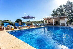 En pool med solstolar och parasoller, en pergola och utsikt över träd.
