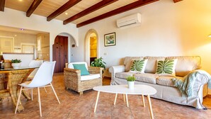 A spacious living area with a dining table, wicker chairs, a sofa with decorative pillows, and a potted plant. - Es Recer by dracmallorca (Santanyi)