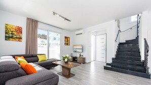 A modern living room with a grey sofa, a wooden coffee table, and a staircase leading to another floor. - Green Bay Villa #15 - Charming Green Bay Getaway (Protaras)