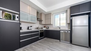 A modern kitchen with dark cabinetry, stainless steel appliances, and a large window providing natural light. - Green Bay Villa #15 - Charming Green Bay Getaway (Protaras)