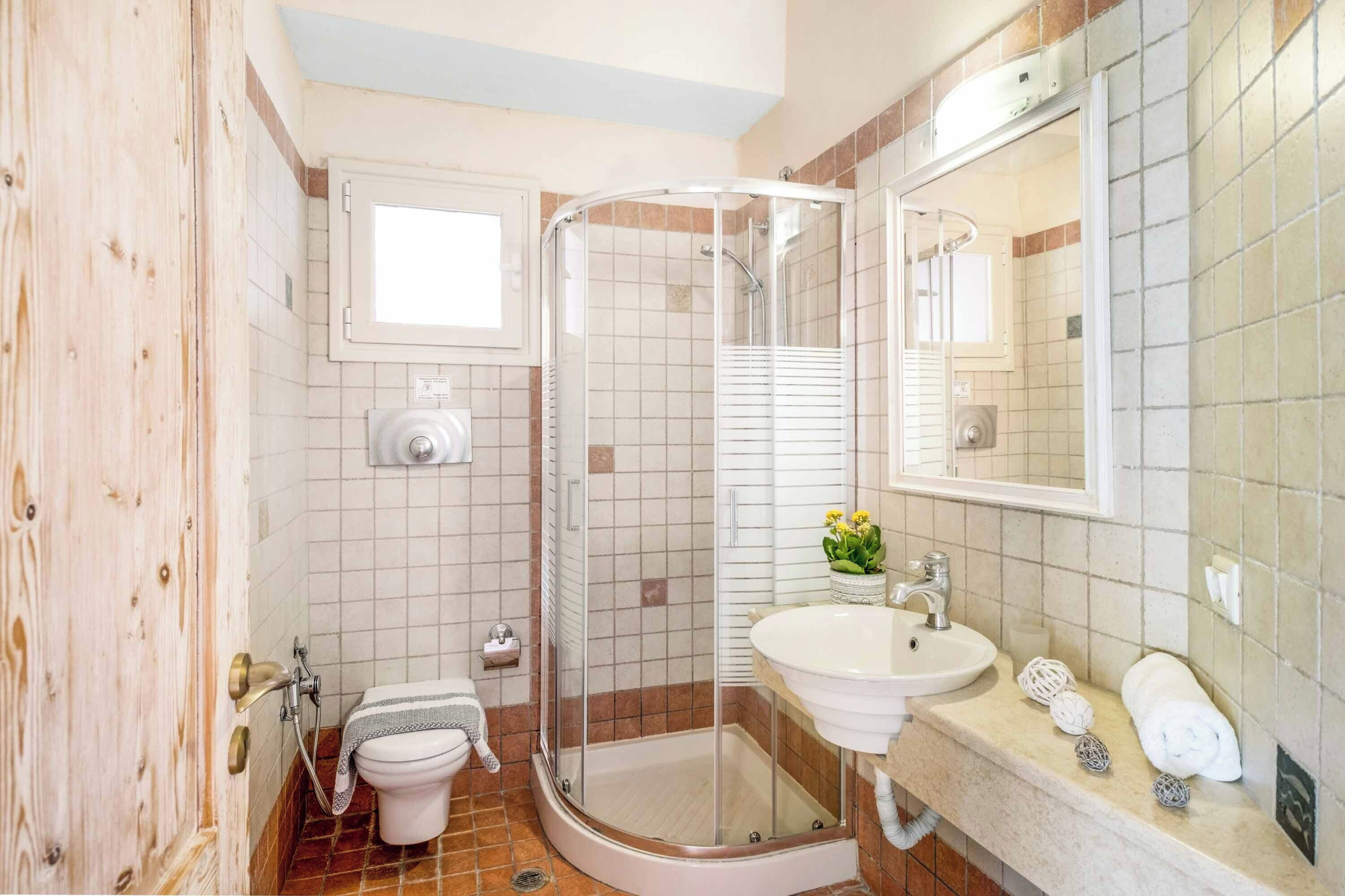 A bathroom with a glass-enclosed shower, a sink, a toilet, and a mirror.