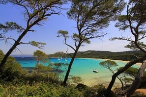 Paisatge costaner amb aigües turqueses cristal·lines, embarcacions i una platja sorrenca envoltada d'arbres.
