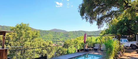 A wooden deck with a pool, lounge chairs, and a view of a mountainous landscape.