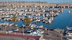 Un puerto deportivo con numerosas embarcaciones amarradas, un paseo peatonal y un área de estacionamiento.