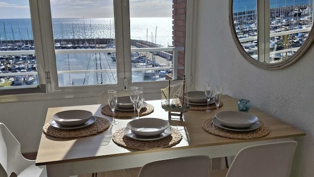 Un comedor con vista a un puerto deportivo, un espejo redondo en la pared y una mesa servida con platos y vasos.