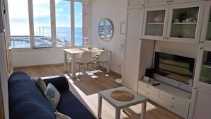 Una sala luminosa con vistas al mar, un comedor y un mueble para la televisión.