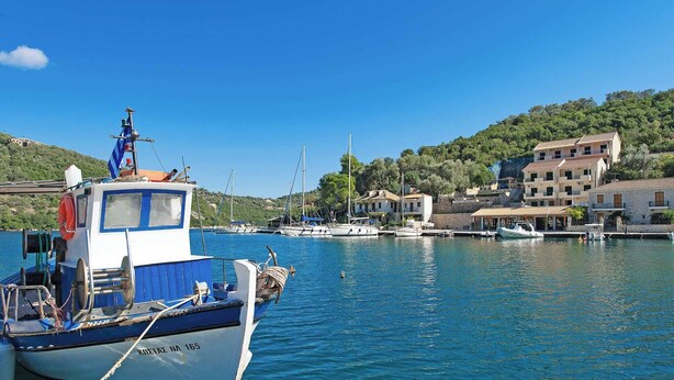 Un port de plaisance avec des bateaux amarrés, un bâtiment doté d’un toit en tuiles et une colline en arrière-plan.