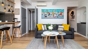 Sala de estar moderna com sofá cinzento, almofadas amarelas, mesa de centro com um livro e um copo, e um quadro na parede.