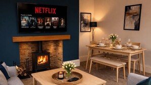 Ett mysigt vardagsrum med en öppen spis, ett matbord för fyra personer och en platt-TV som visar populära serier från Netflix.