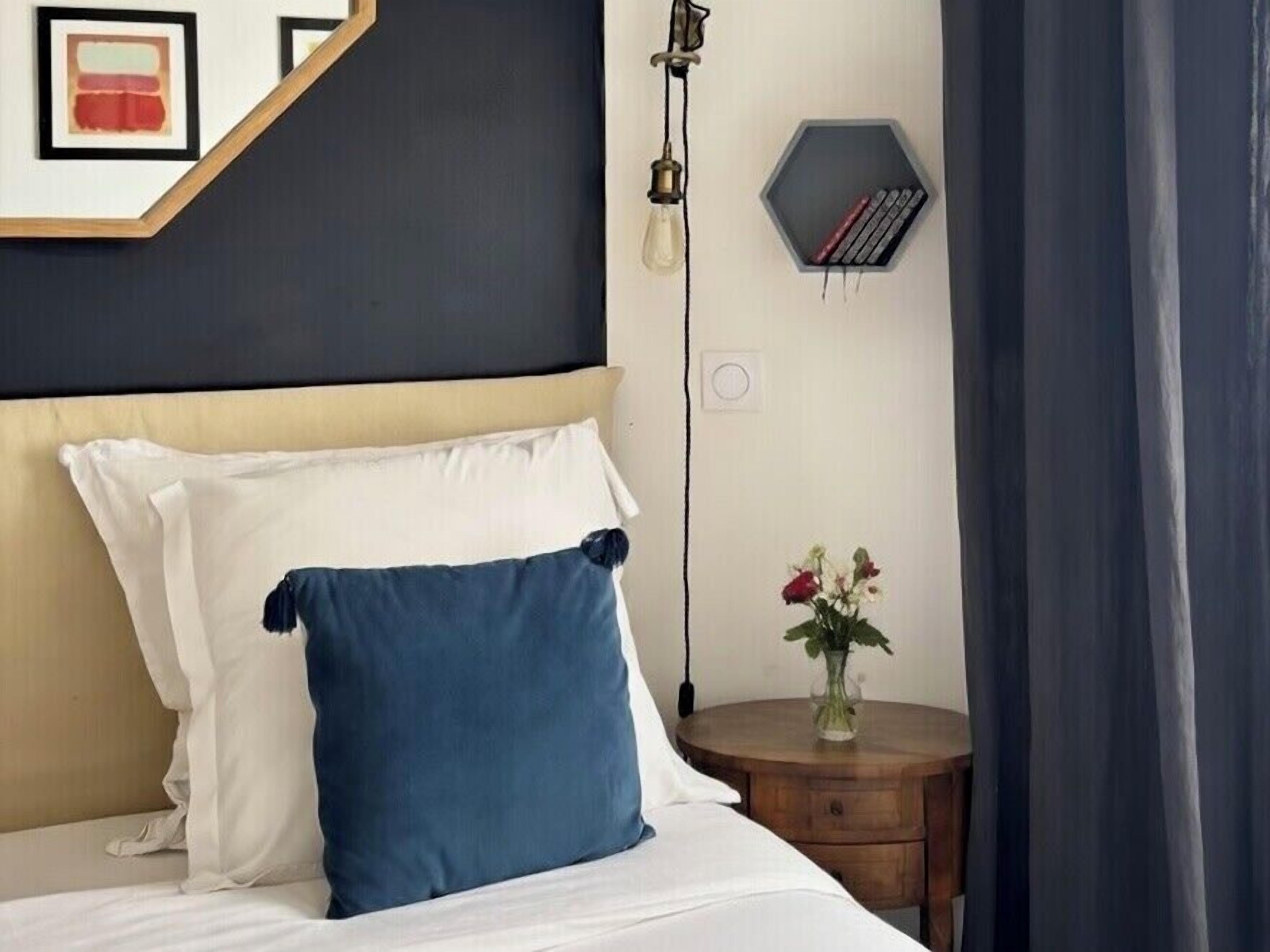Een hotelkamer met een bed, een nachtkastje met een bloevas en een wandlamp.