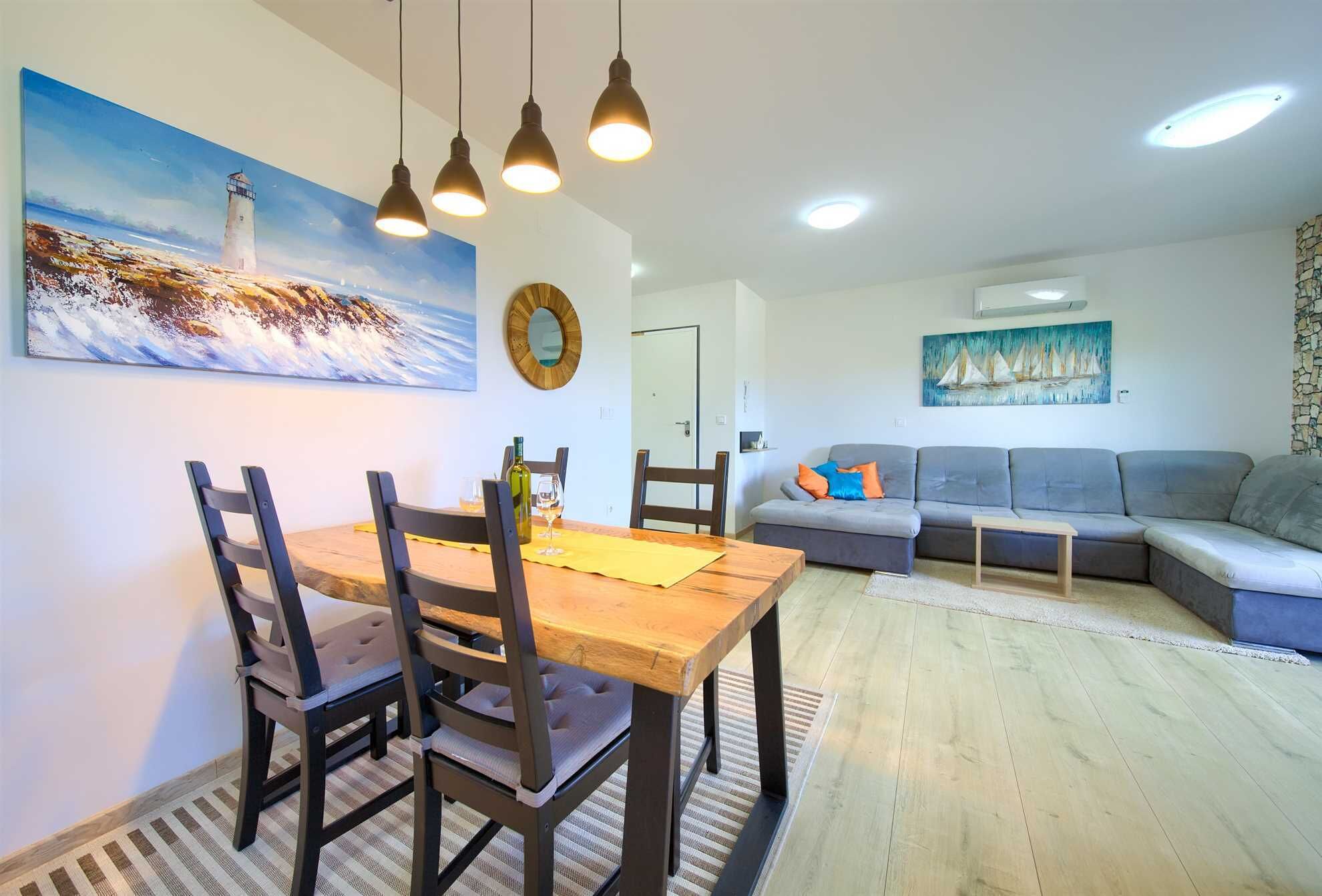 A dining area with a wooden table and chairs, a gray sofa, and a painting of a lighthouse.